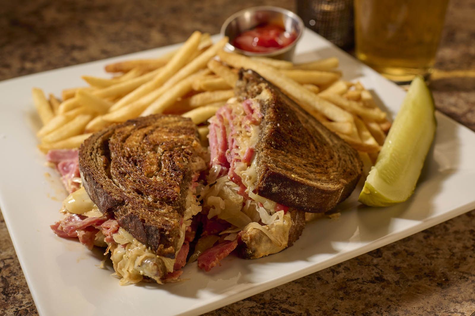 Sandwich served with pickle, french fries, and a beer